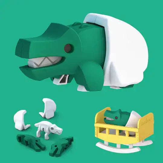 a plastic green baby crocodile in a white 2 part diaper and below shows the 5 parts that make the baby crocodile, with a picture of the plastic baby crocodile in the diaper, sitting in the rocking cradle to the right. 